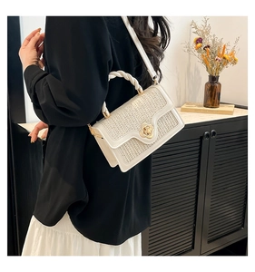 Detail view of woven straw handbag featuring golden floral metal lock and twisted handle