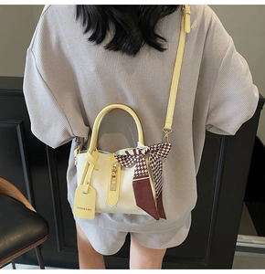 Dettaglio della texture in pelle di litchi della borsa a secchiello con manico giallo e foulard