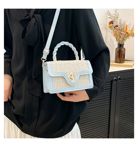 Detail of light blue crossbody bag featuring woven beige flap and golden clover clasp