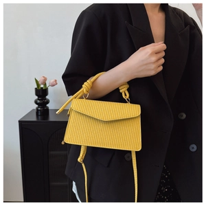 Détail de la texture tissée jaune du sac avec poignée décorative nouée et finitions dorées