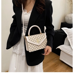 Detail of beige monogram square bag with gold lock worn over a black blazer