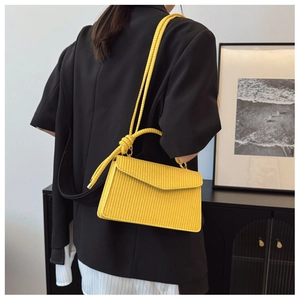 Détail du sac bandoulière tissé jaune avec sangle à nœud décoratif sur un blazer noir