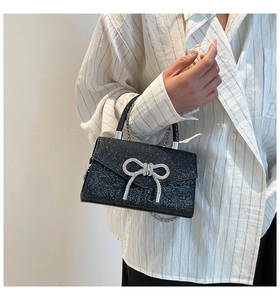Détail d'un sac à main noir à paillettes avec un nœud en strass brillant et une chaîne