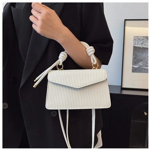 Détail du sac enveloppe blanc à texture chevrons avec poignée torsadée et boucles dorées