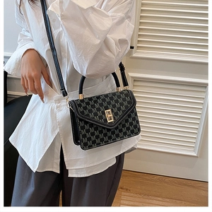 Close-up of black crossbody bag with M-letter pattern and gold clasp on a model