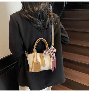 Elegante borsa a secchiello beige con manici marroni e sciarpa indossata da una modella
