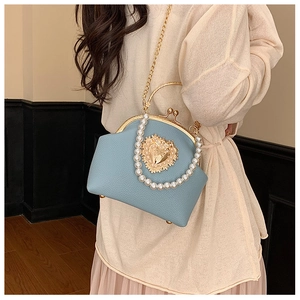 Detail of light blue leather shell bag with gold heart logo and pearl handle accents