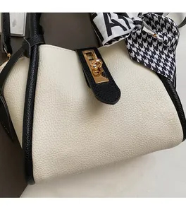 Dettaglio borsa a secchiello bicolore crema e nera con chiusura dorata e foulard di seta