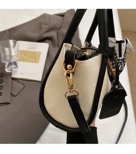 Dettaglio borsa a secchiello in pelle martellata con finiture dorate e foulard pied-de-poule