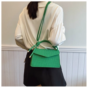 Détail d'un sac bandoulière tressé vert avec poignée et sangle nouée porté par un mannequin