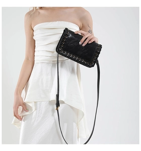 Detail of woven black leather bag with gold metal rings and adjustable shoulder strap
