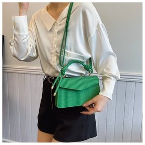 Détail d'un sac à main vert tressé avec poignée nouée et bandoulière tressée assortie