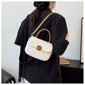 White textured crossbody bag with brown buckle shown on model wearing black blazer