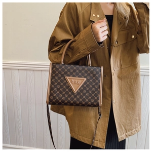 Macro detail of brown monogram tote bag showing textured leather handles and logo plaque