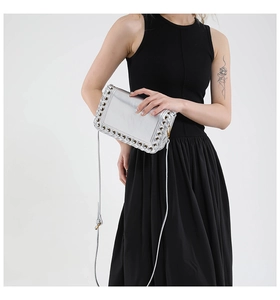 Detail of silver metallic crossbody bag with grommet edges on a minimalist background
