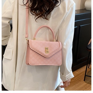 Detail view of a pale pink textured handbag with golden lock and adjustable strap