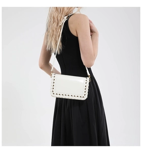 Detail of white leather shoulder bag featuring metal eyelets and woven trim accents