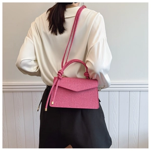 Détail du sac tressé rose fuchsia avec une poignée décorative en forme de gros nœud