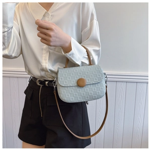 Detail of light blue crossbody bag with textured grid pattern and brown circular accent