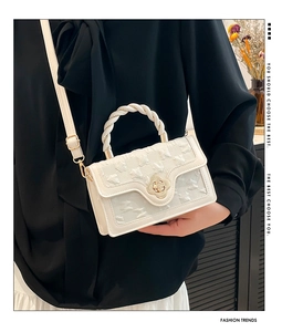 Detail of cream square handbag showing textured fabric, flower clasp, and braided handle