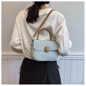 Detail of mint green crossbody bag with checkered texture and brown round buckle on model