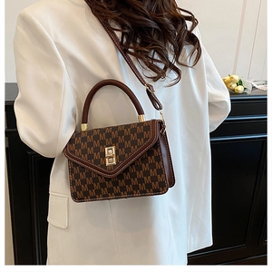 Brown handbag with 'M' pattern and metal lock shown on a model in white blazer