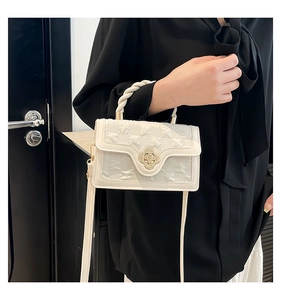 Detail of cream crossbody bag with floral gold clasp and embossed textured surface
