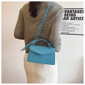 Sac bandoulière tissé bleu avec poignée nouée et rabat en V porté dans un cadre artistique