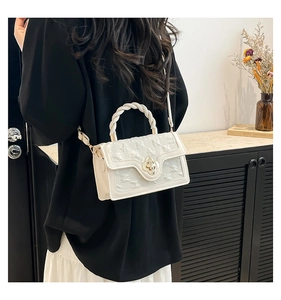 Detail of cream crossbody bag featuring embossed texture and a gold floral metal clasp