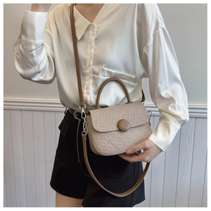 Model wearing a beige embossed handbag with brown handles and a round decorative buckle
