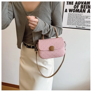 Detailed view of pink embossed crossbody bag featuring a brown round magnetic clasp and strap