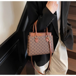 Gros plan du sac à main marron à motif M avec boucles dorées sur un escalier en bois