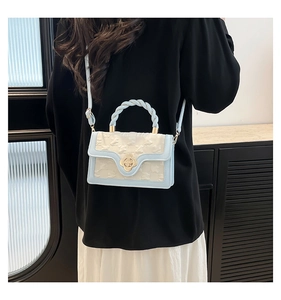 Close-up of sky blue flap bag with gold flower lock and twisted woven handle