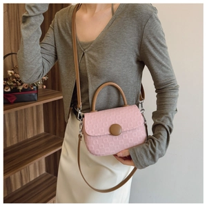 Detailed shot of pink quilted handbag featuring brown top handle and circular buckle closure
