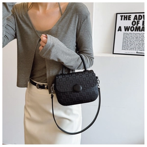 Detail of black embossed crossbody bag with large round buckle worn by model