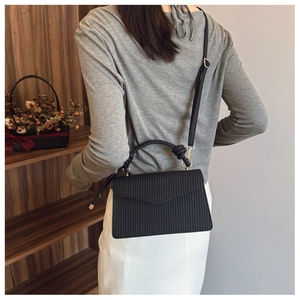 Détail du sac bandoulière noir texturé avec rabat en V et poignée tressée sur modèle