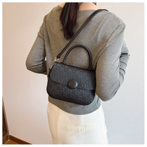 Detail view of black embossed crossbody bag showing geometric pattern and silver hardware