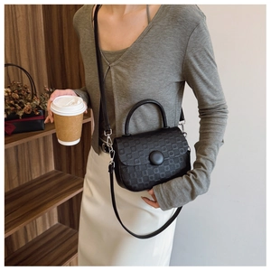 Detail of black textured crossbody bag featuring a round decorative buckle and slim strap