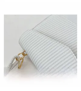 Détail de la texture tressée blanche du sac avec fermoir doré et poignée nouée élégante