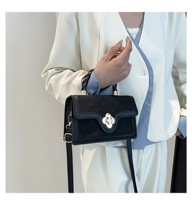 Detail of black embossed leather handbag with golden floral clasp and woven handle