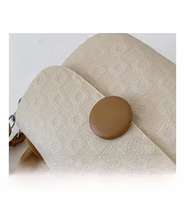 Detail of cream quilted fabric texture and brown leather decorative button on a shoulder bag