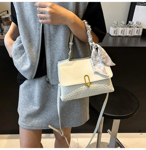 Dettaglio della borsa bianca intrecciata con fibbia dorata e foulard in seta con stampa orso