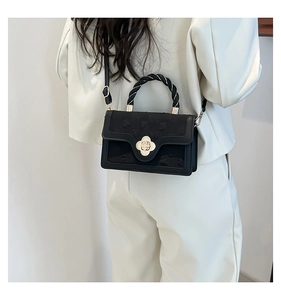 Detail of black crossbody bag with gold clover lock and woven handle worn by model