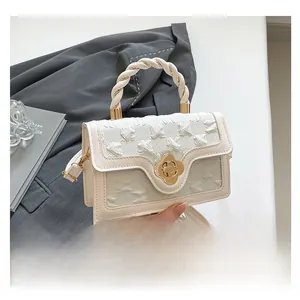 Detail of floral texture and gold flower clasp on beige crossbody bag with braided handle