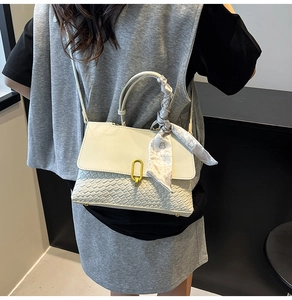 Dettaglio borsa a mano intrecciata con fibbia a U dorata e foulard di seta sulla maniglia