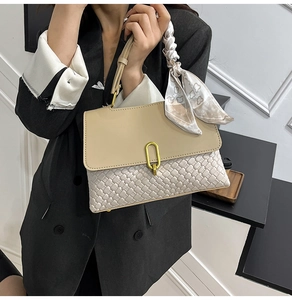 Dettaglio di una borsa beige intrecciata con fibbia dorata e manico con foulard in seta