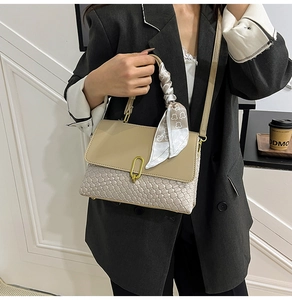 Dettaglio della borsa intrecciata beige con fibbia dorata e foulard in seta elegante