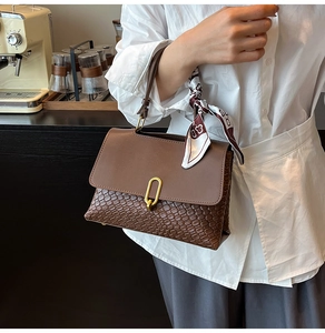 Dettaglio della trama intrecciata e fibbia dorata su borsa marrone con foulard decorativo