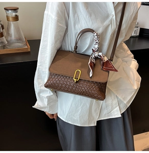 Dettaglio borsa marrone intrecciata con fibbia dorata e foulard decorativo in seta