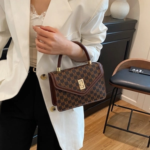 Brown leather handbag with M-pattern print and gold rotating lock in a warm indoor setting